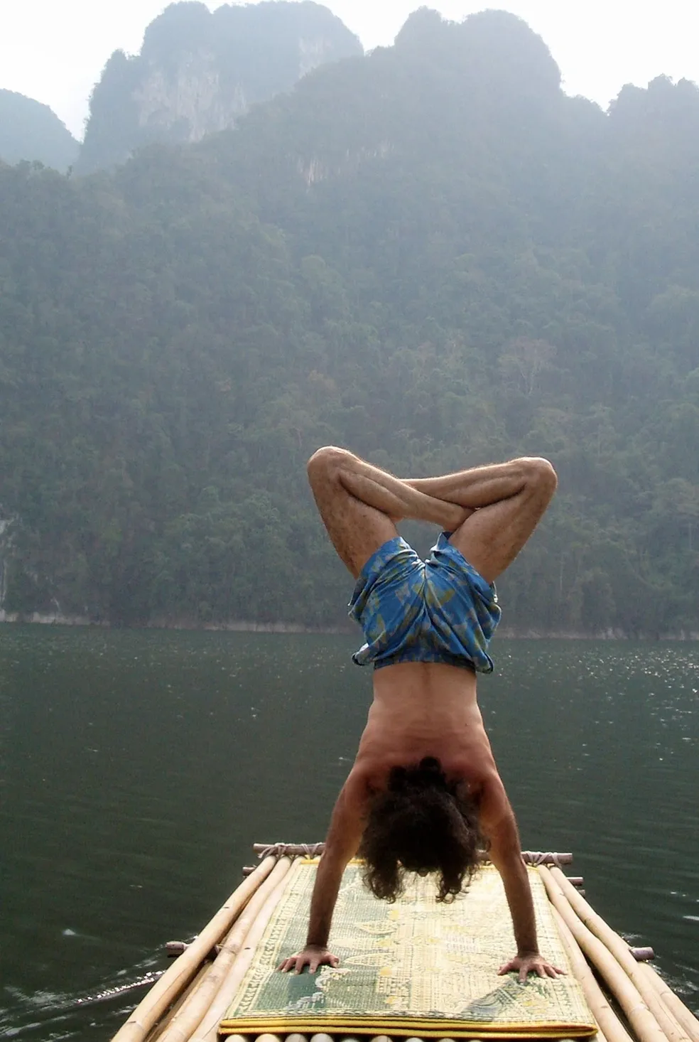 Danny Paradise in a lotus handstand on a bamboo raft, on a jungle lake